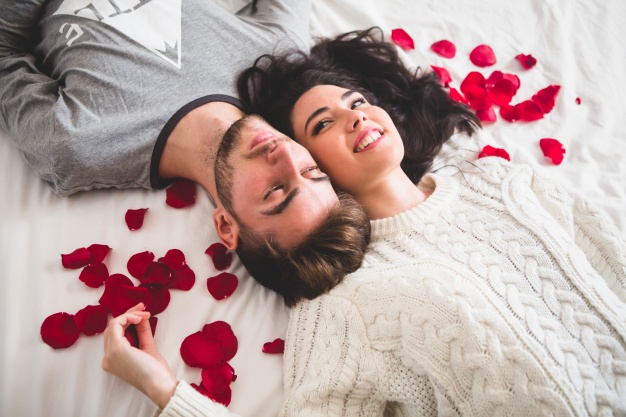 couple-lying-on-bed-head-with-head-surrounded-by-rose-petals_23-2147595997